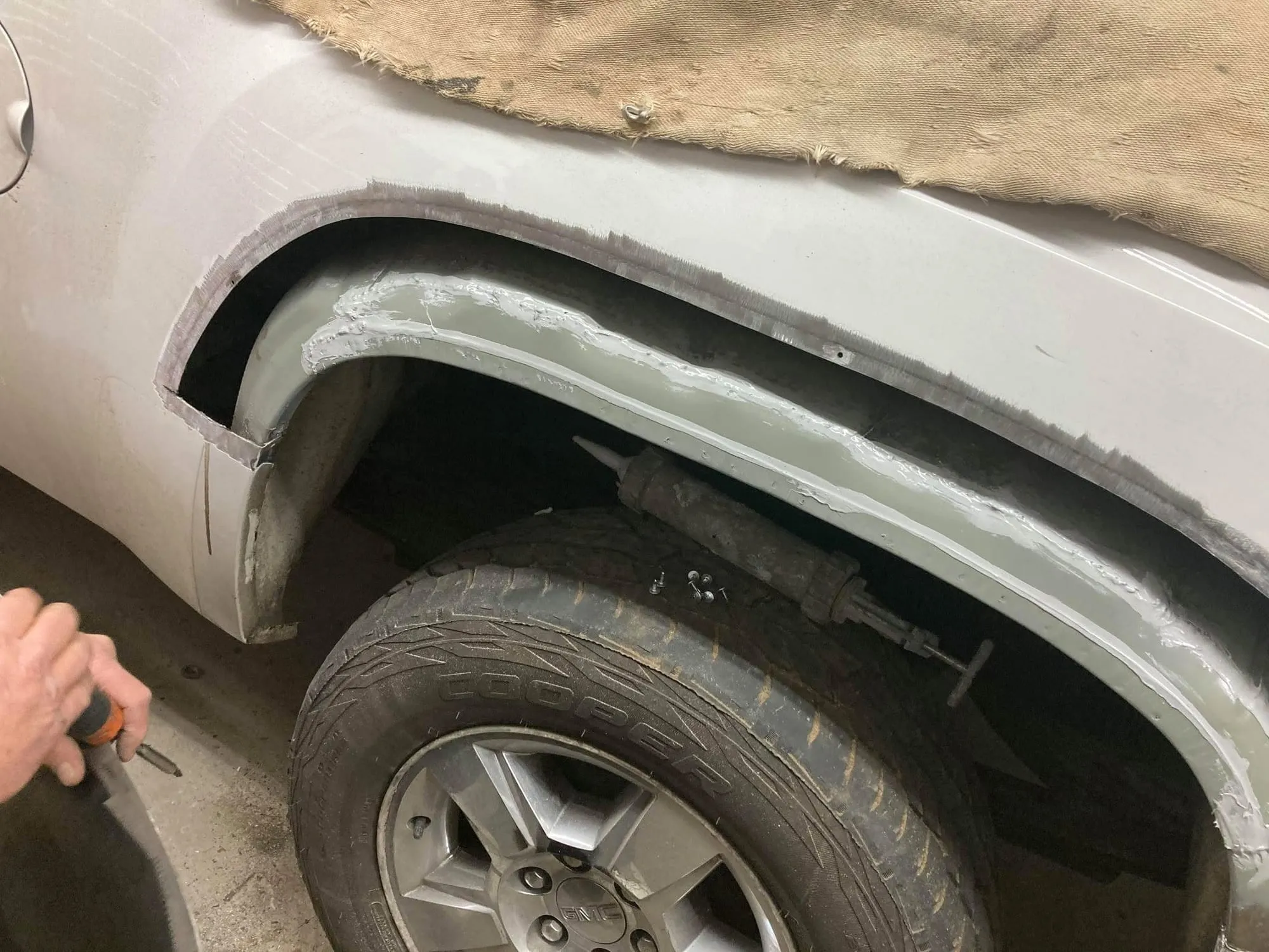 Body filler being shaped on the rear wheel arch of a silver GMC Sierra
