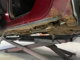 Rusted-through rocker panel on a red GMC Terrain on the lift